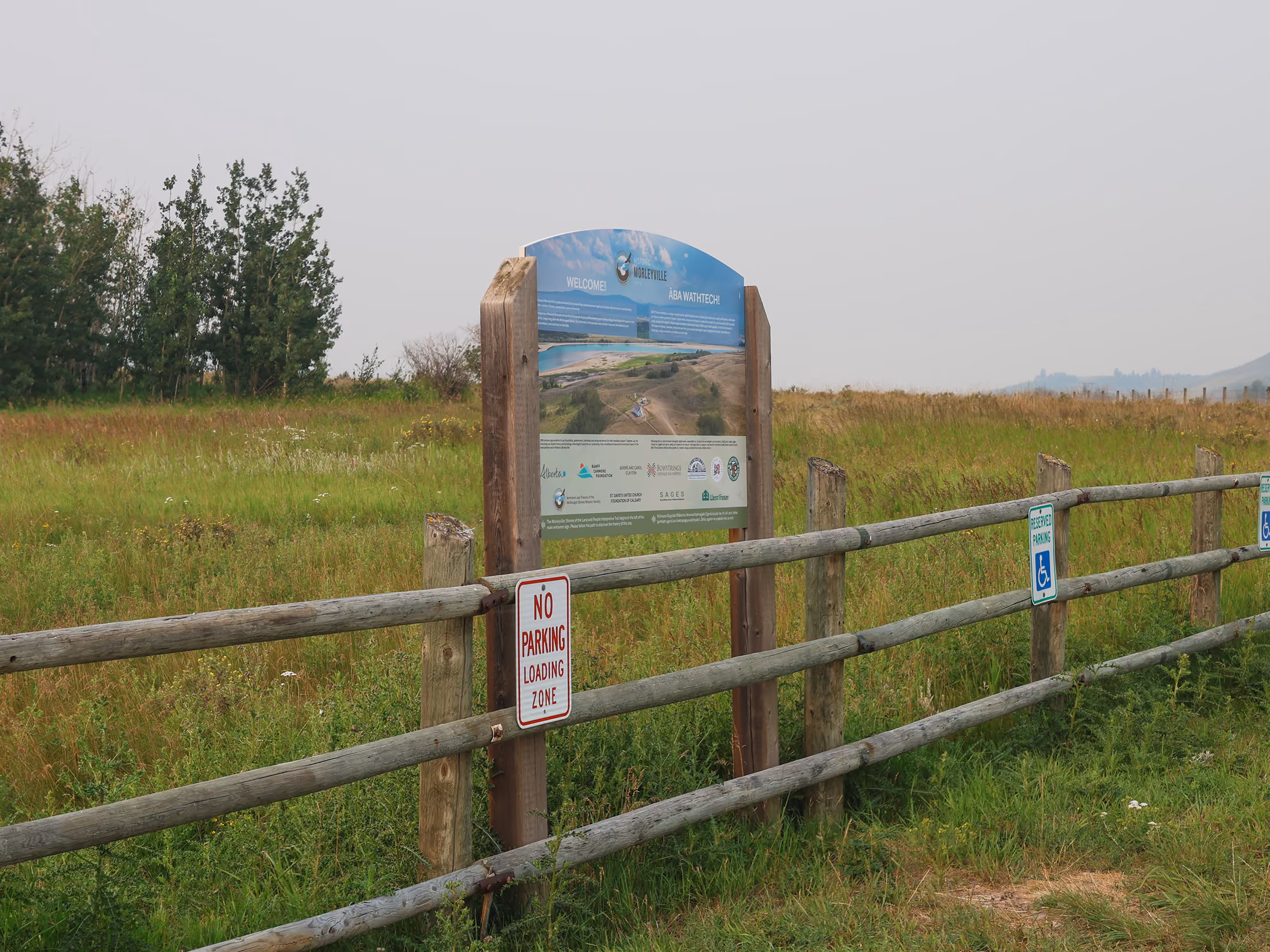Welcome and site information panel mounted near the fenced entrance with reserved parking signage.