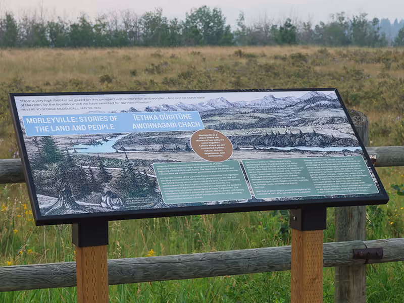 "Morleyville: Stories of the Land and People" interpretive panel mounted along a wood rail fence.