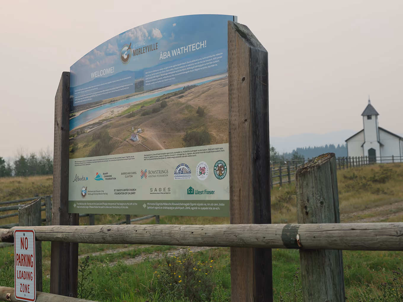 Welcome sign for Historic Morleyville mounted on wood posts with the church visible in the distance.