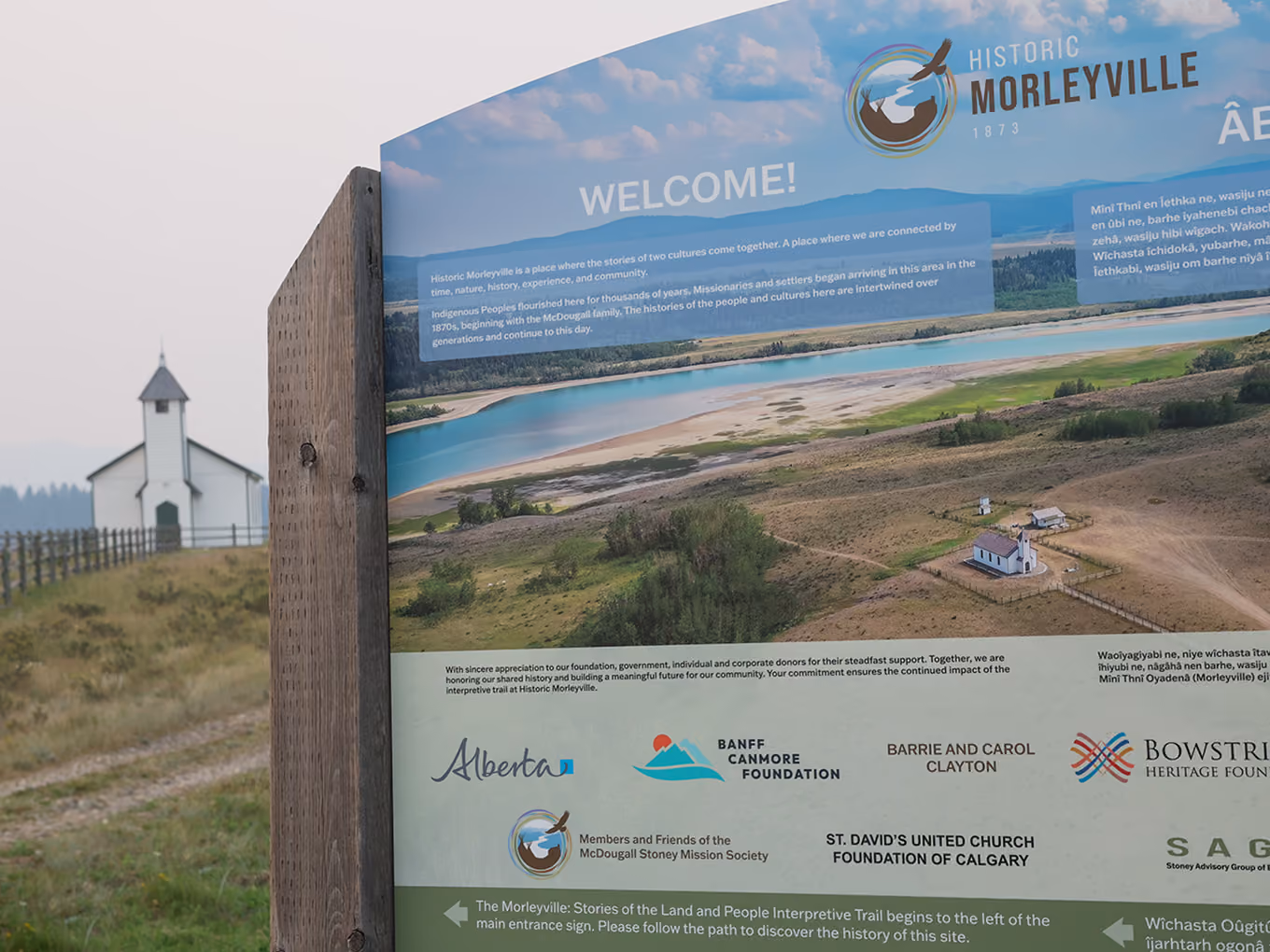 Close-up corner detail of the Historic Morleyville donor recognition sign with the church framed in the background.