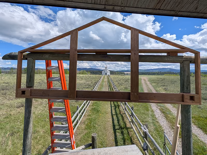 exhibit Installer securing the entrance arch sign panel on site using a ladder and lift platform.