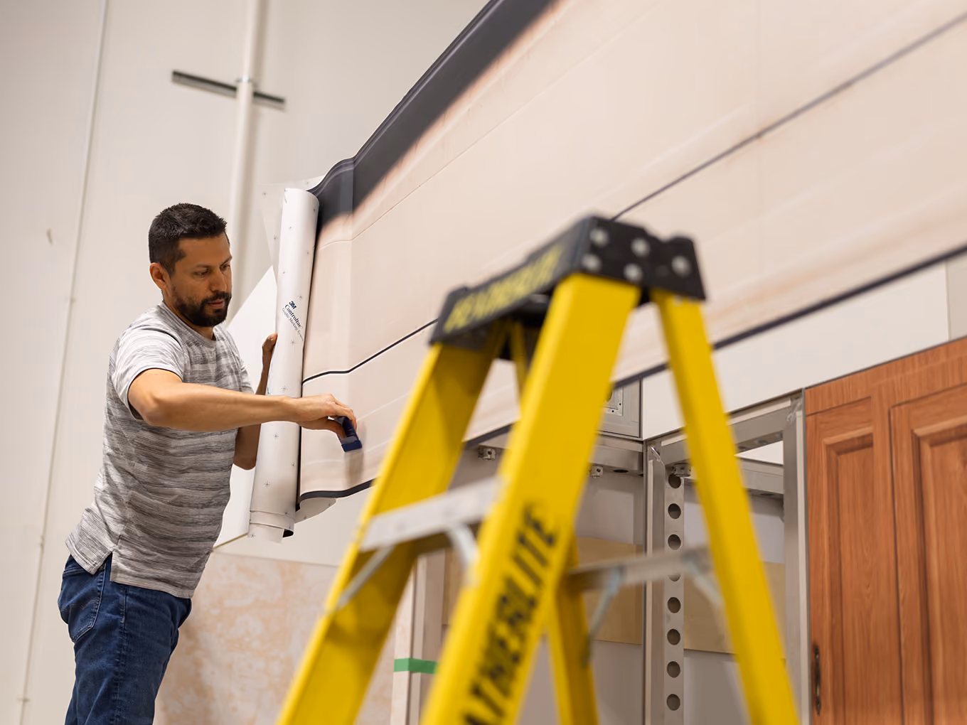 An installer applies a vinyl graphic wrap to the roofline of the custom RV façade on a ladder.