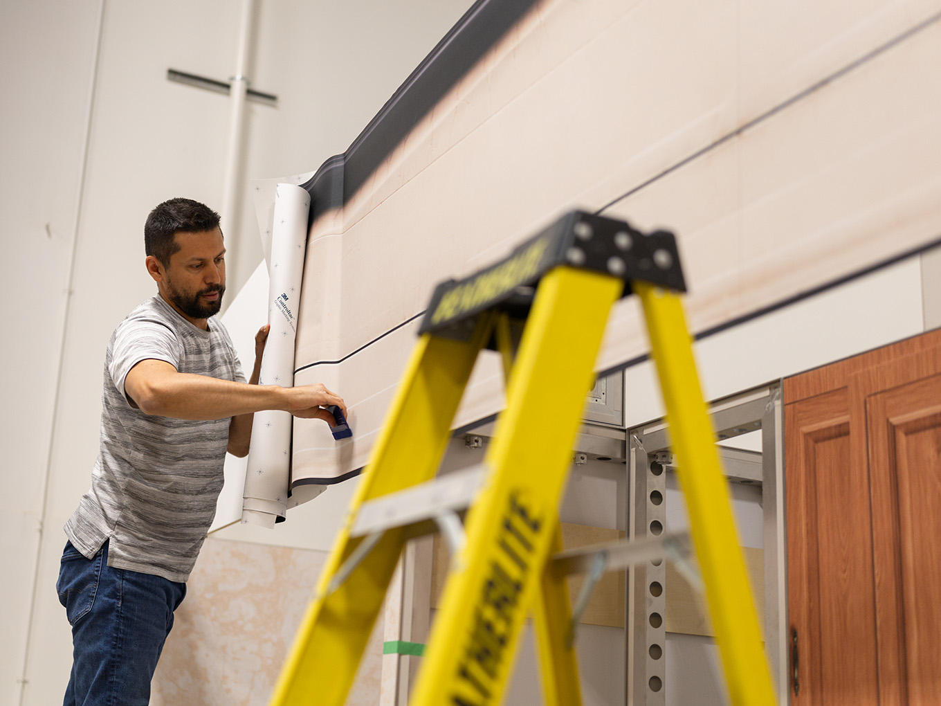 An installer applies a vinyl graphic wrap to the roofline of the custom RV façade on a ladder.