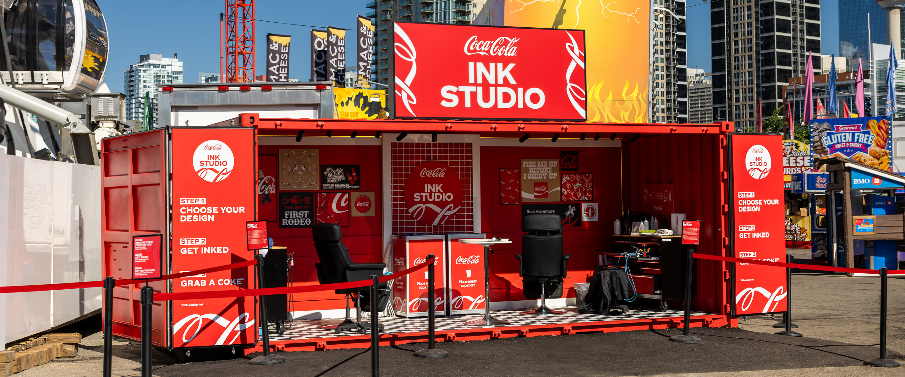 Custom Coca-Cola Ink Studio seacan activation with illuminated signage at the Calgary Stampede against the downtown skyline.