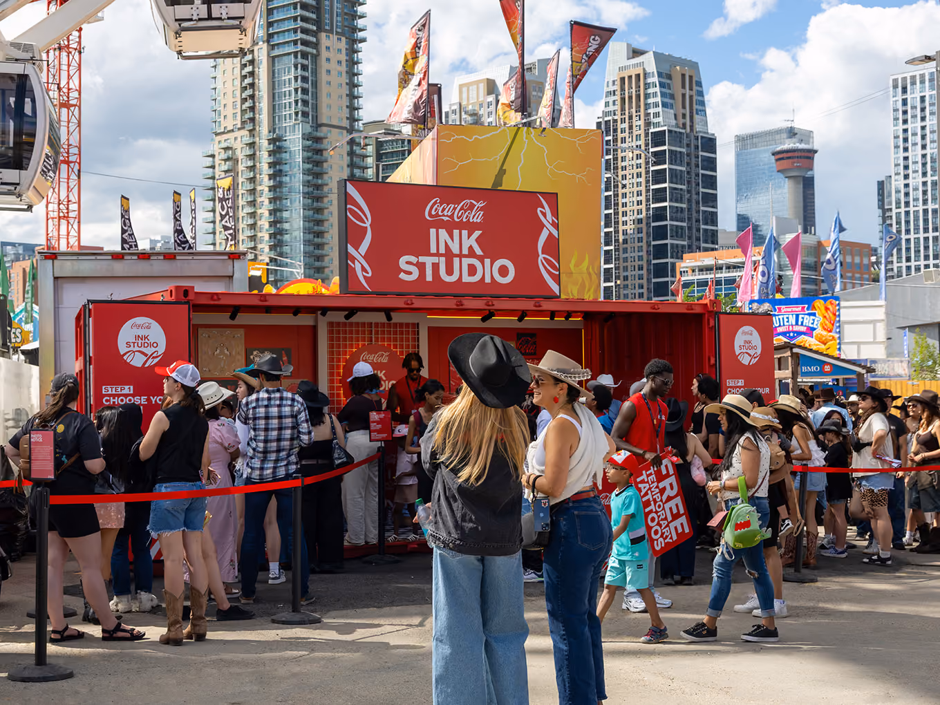 Visitors line up at the Coca-Cola Ink Studio seacan activation during the Calgary Stampede, with the Ferris wheel nearby.