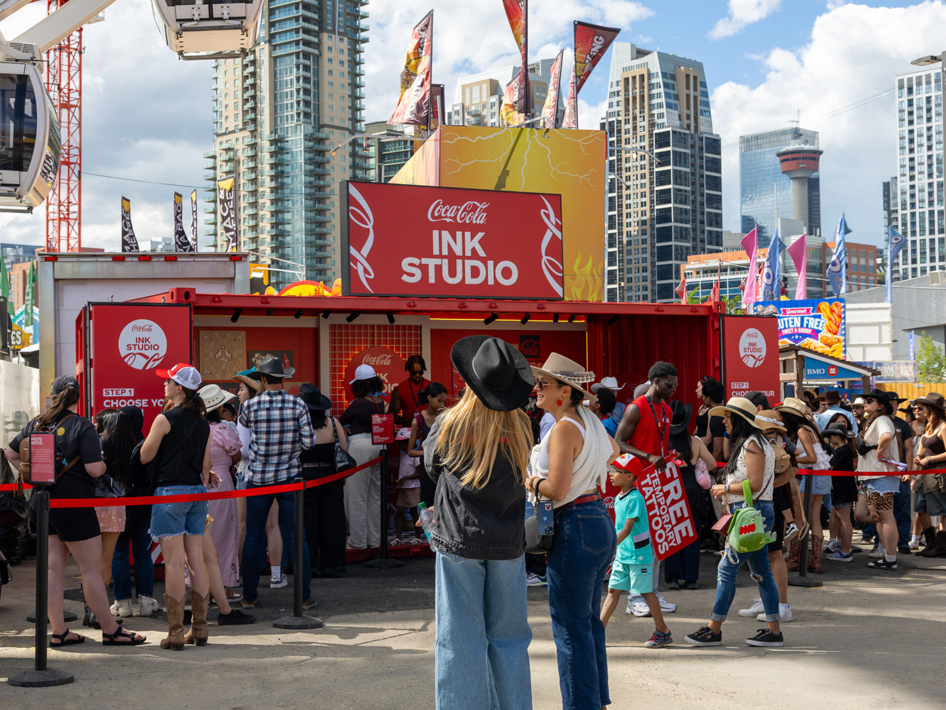 Visitors line up at the Coca-Cola Ink Studio seacan activation during the Calgary Stampede, with the Ferris wheel nearby.