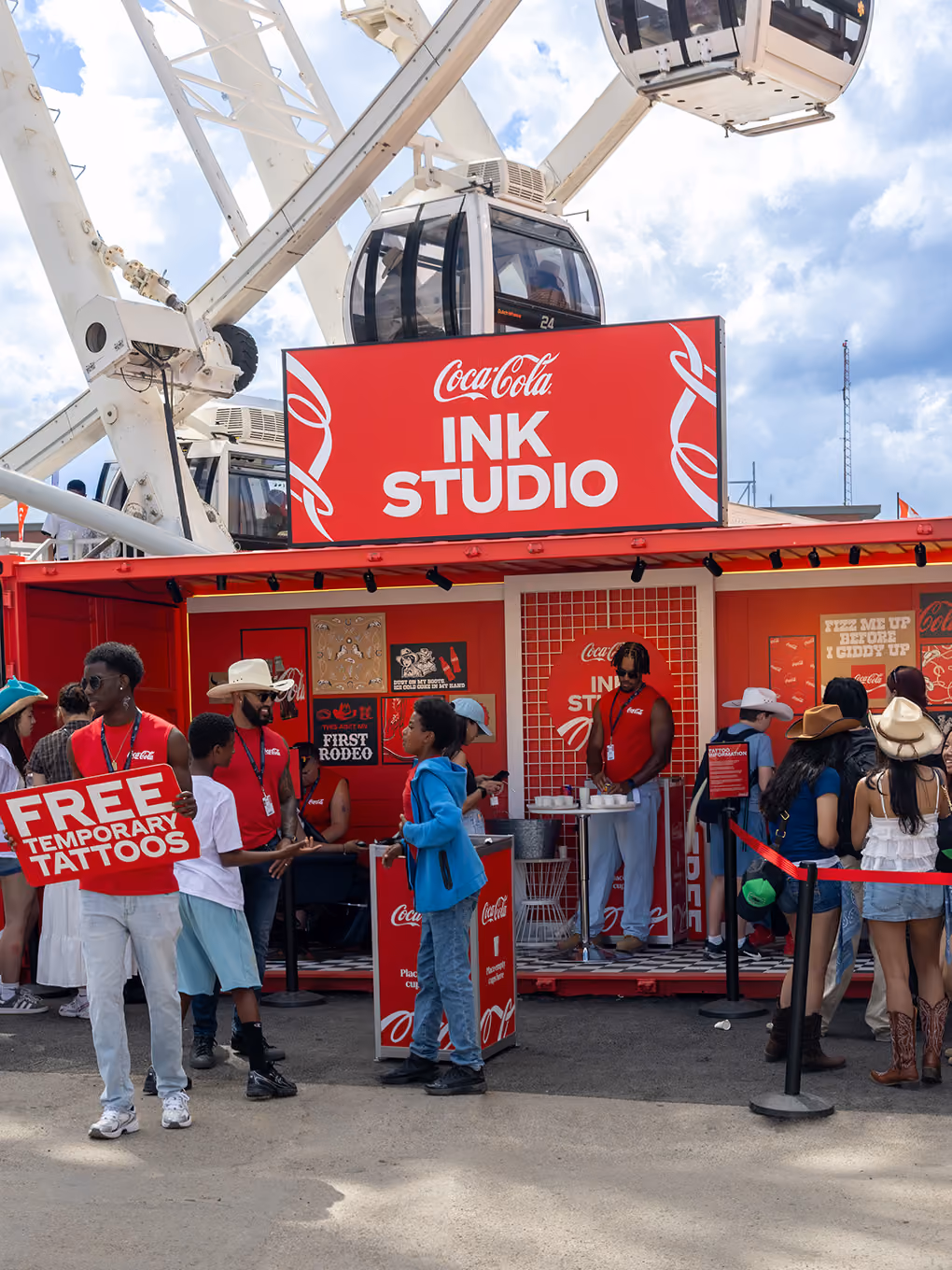 Staff advertising free temporary tattoos in front of the Coca-Cola Ink Studio seacan beneath the Calgary Stampede Ferris wheel.