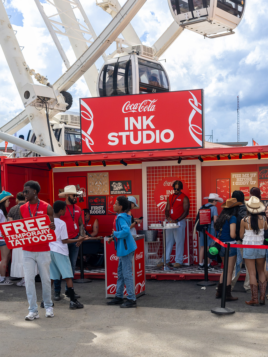 Staff advertising free temporary tattoos in front of the Coca-Cola Ink Studio seacan beneath the Calgary Stampede Ferris wheel.