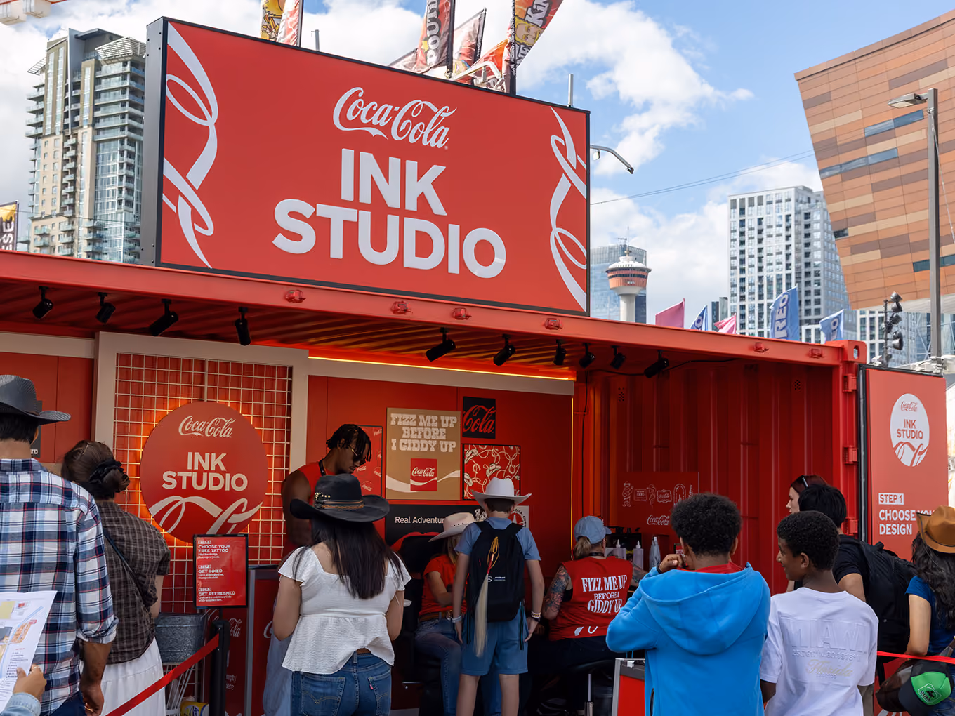Guests line up outside the custom Coca-Cola Ink Studio seacan with the Calgary Tower visible in the skyline.