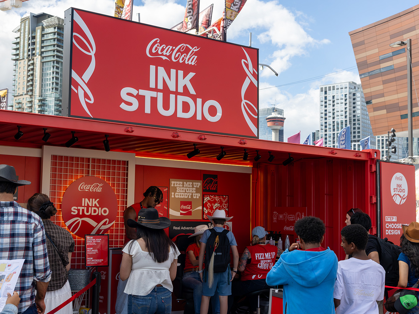 Guests line up outside the custom Coca-Cola Ink Studio seacan with the Calgary Tower visible in the skyline.