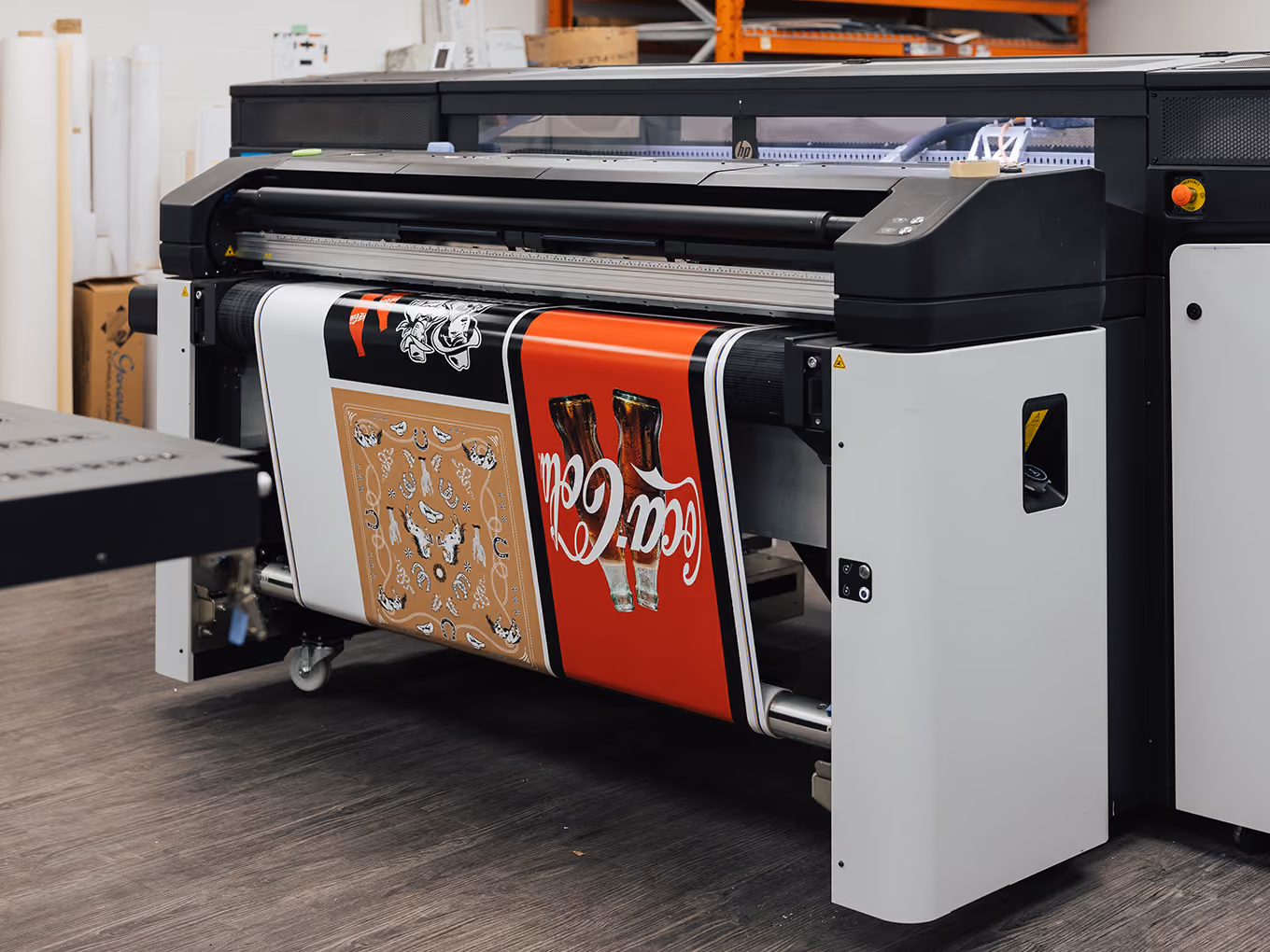 Large-format printer producing custom Coca-Cola cowboy boot graphics for the Ink Studio seacan build.