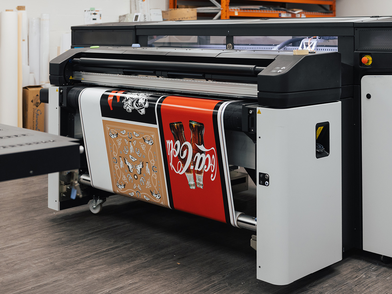 Large-format printer producing custom Coca-Cola cowboy boot graphics for the Ink Studio seacan build.