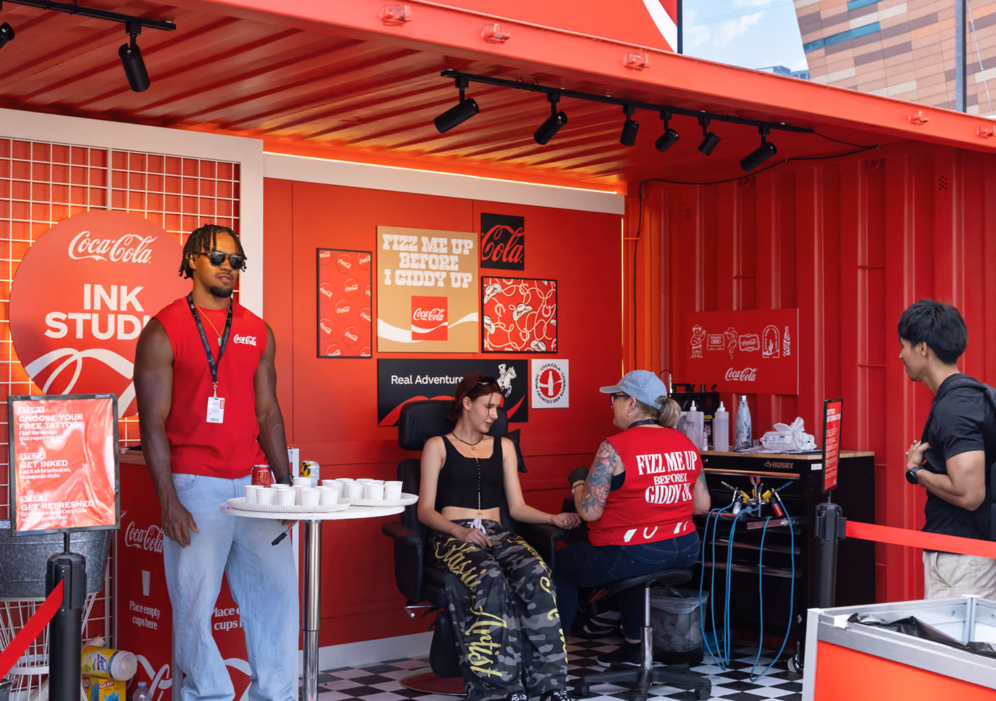 Coca-Cola brand ambassadors and tattoo artist engage a visitor inside the completed Ink Studio seacan.