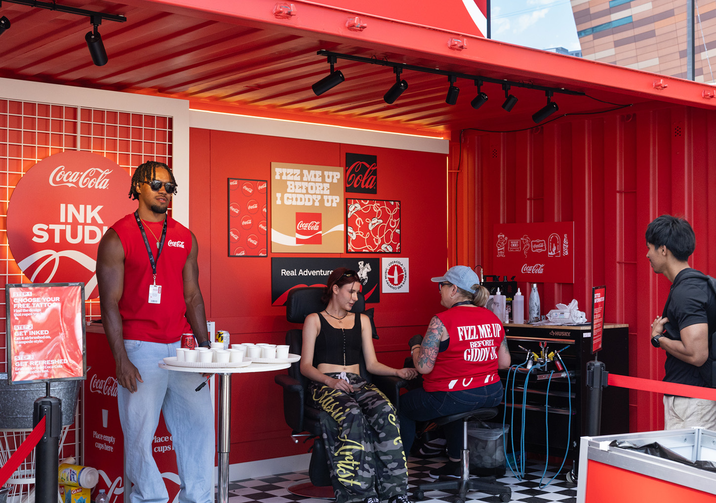 Coca-Cola brand ambassadors and tattoo artist engage a visitor inside the completed Ink Studio seacan.