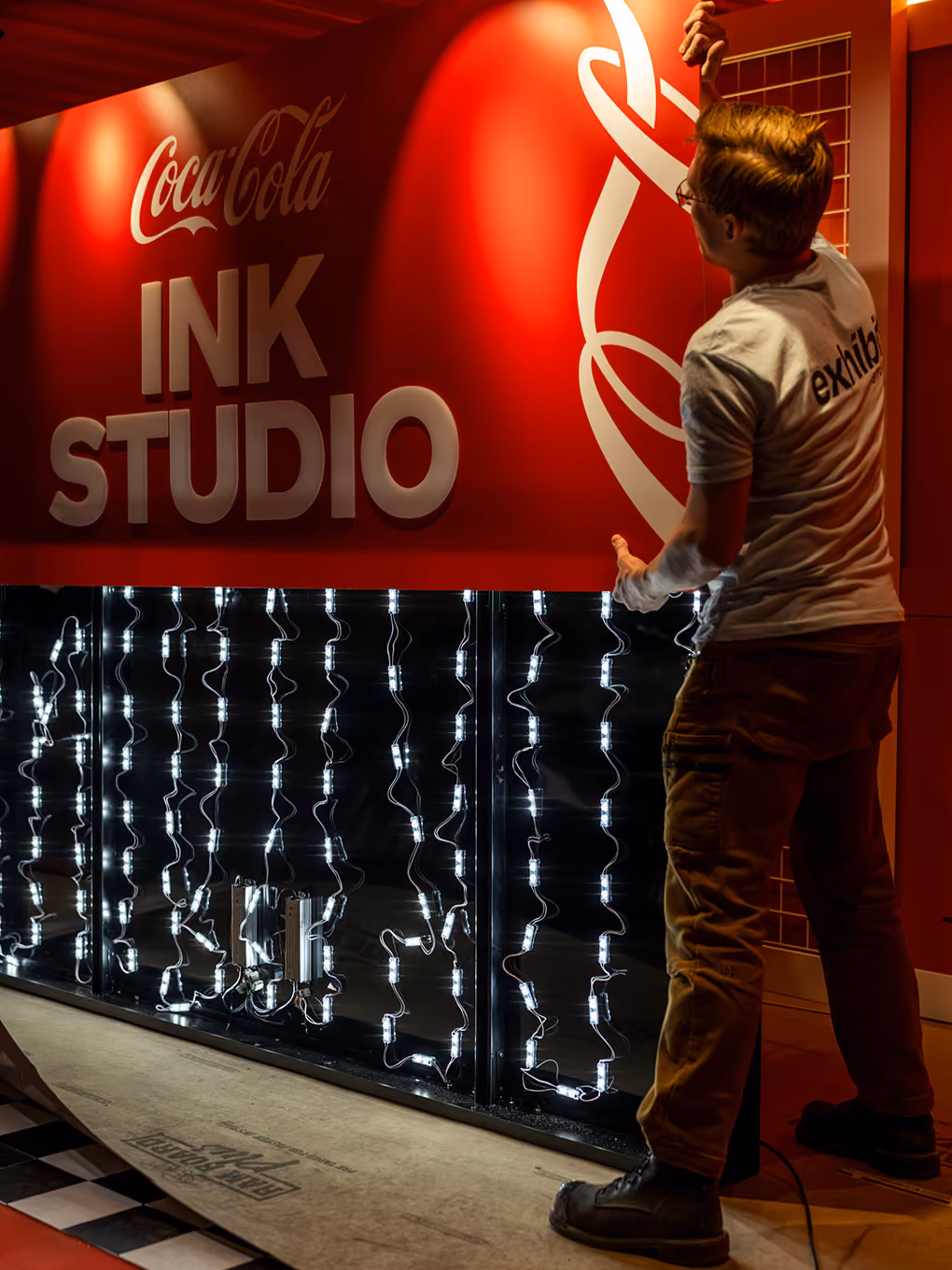 Exhibit Studio team member wiring integrated LED lighting behind the Coca-Cola Ink Studio sign.