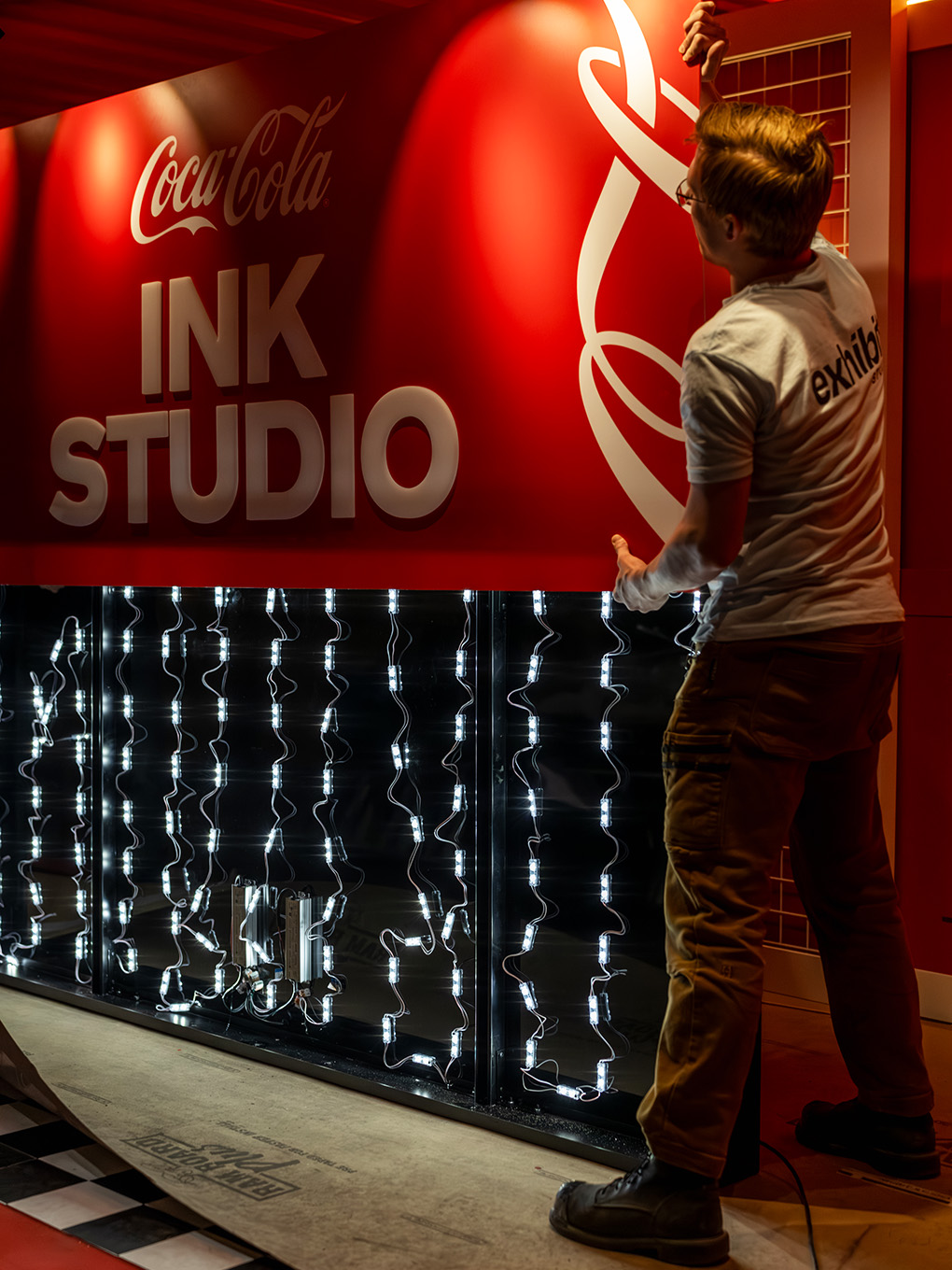 Exhibit Studio team member wiring integrated LED lighting behind the Coca-Cola Ink Studio sign.