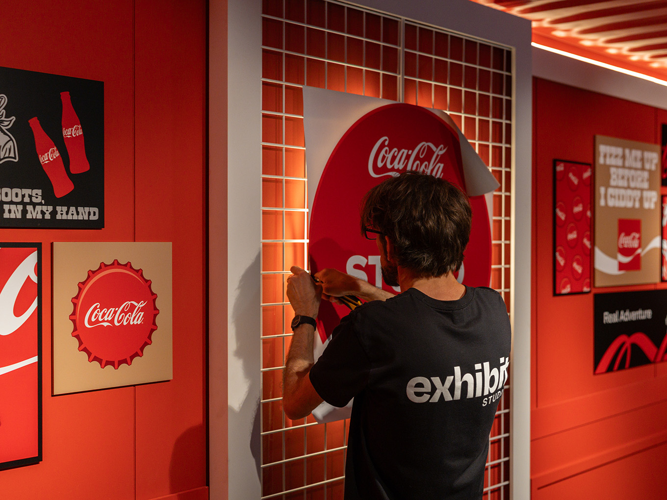 Exhibit Studio team member installing custom Coca-Cola signage onto the seacan's illuminated gridwall.