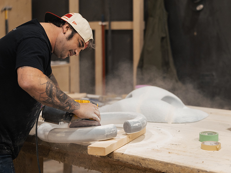 Exhibit Studio fabricator sanding a custom-shaped foam component for the GMC parade vehicle display.