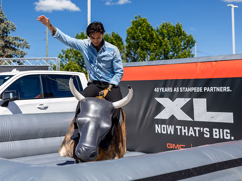 Guest rides a mechanical bull in front of branded GMC signage at a Calgary Stampede event.