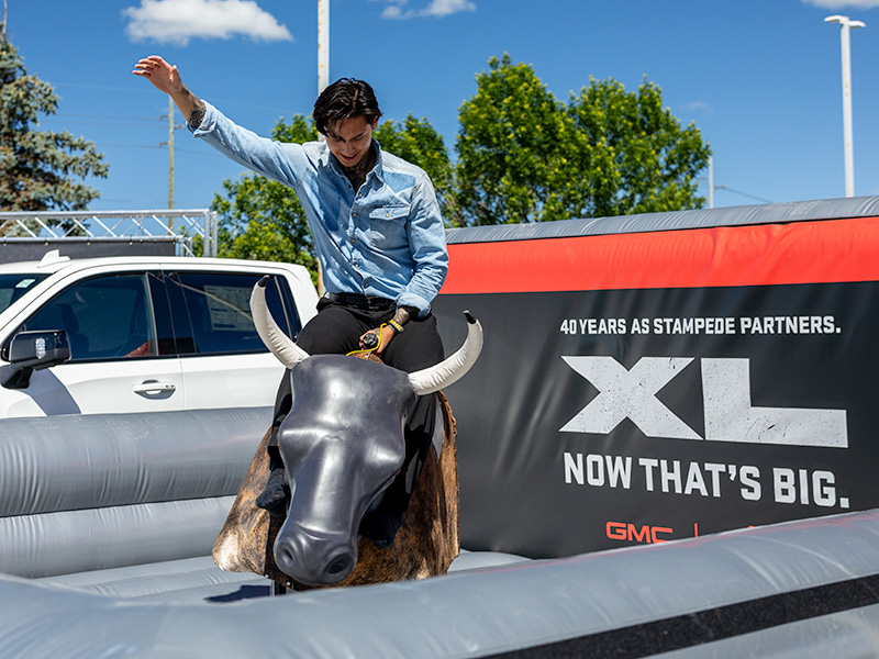 Guest rides a mechanical bull in front of branded GMC signage at a Calgary Stampede event.