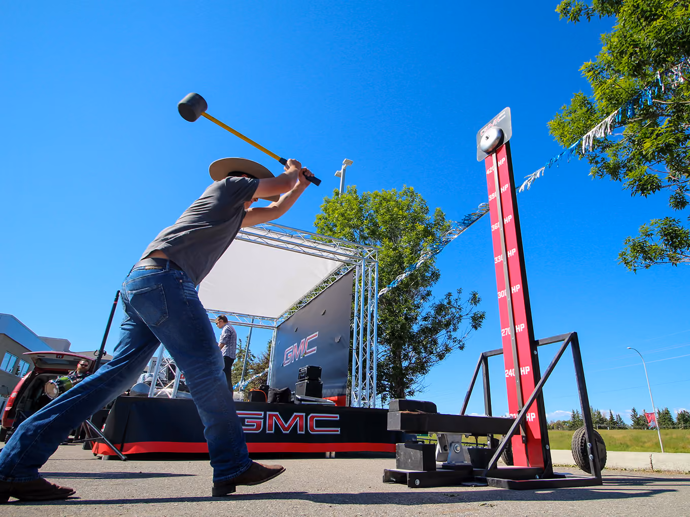 Guest swings a mallet at a custom GMC-branded high striker game beside the event stage.