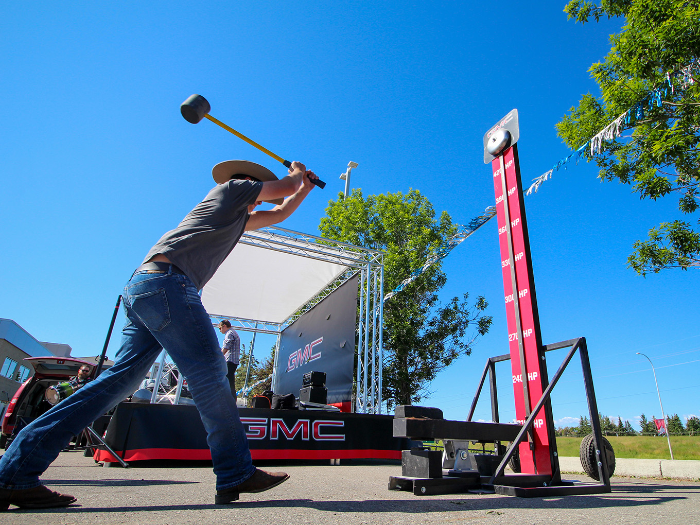 Guest swings a mallet at a custom GMC-branded high striker game beside the event stage.