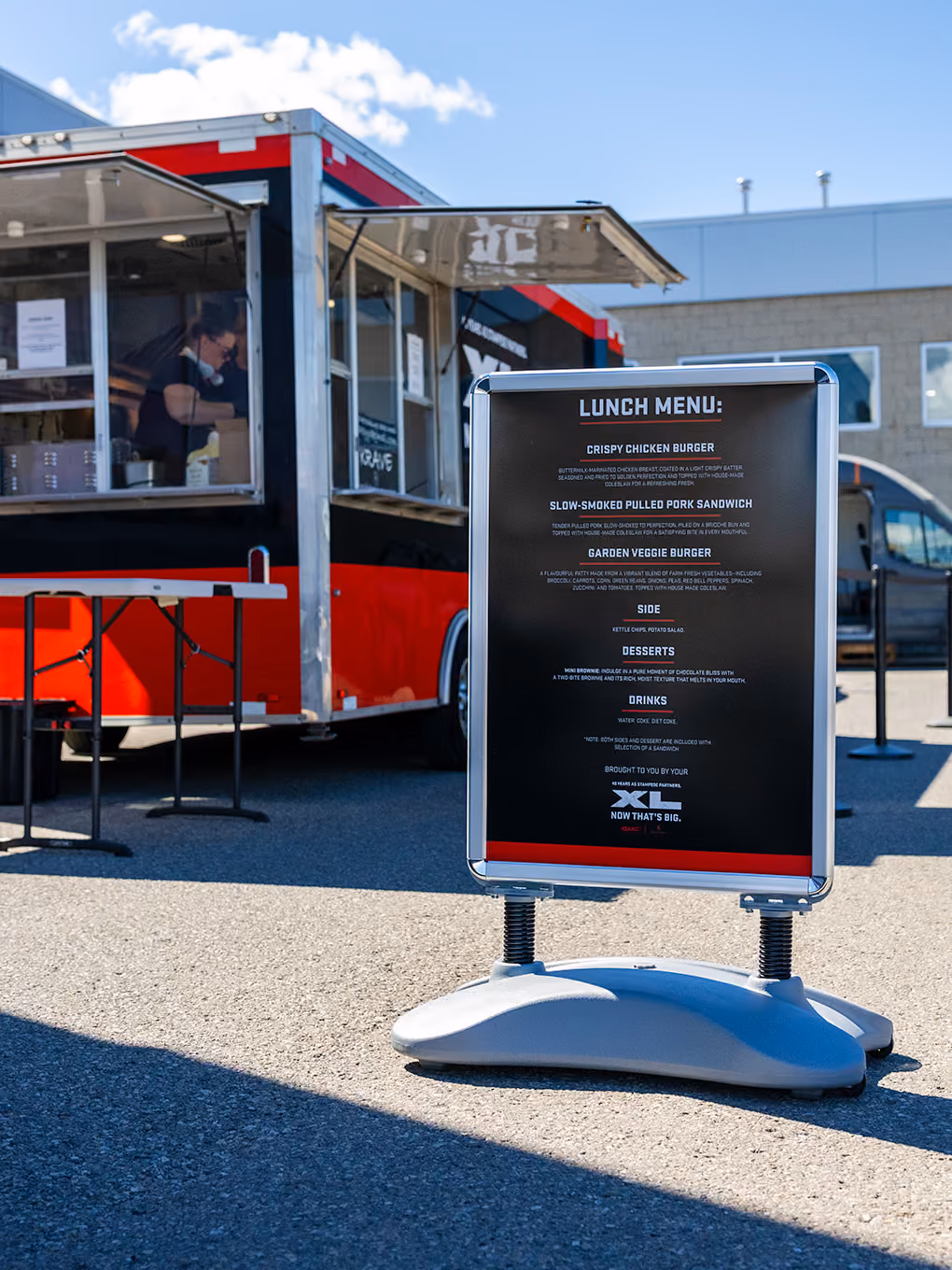Lunch menu signage beside a custom-decaled GMC XL food trailer at a Stampede event.