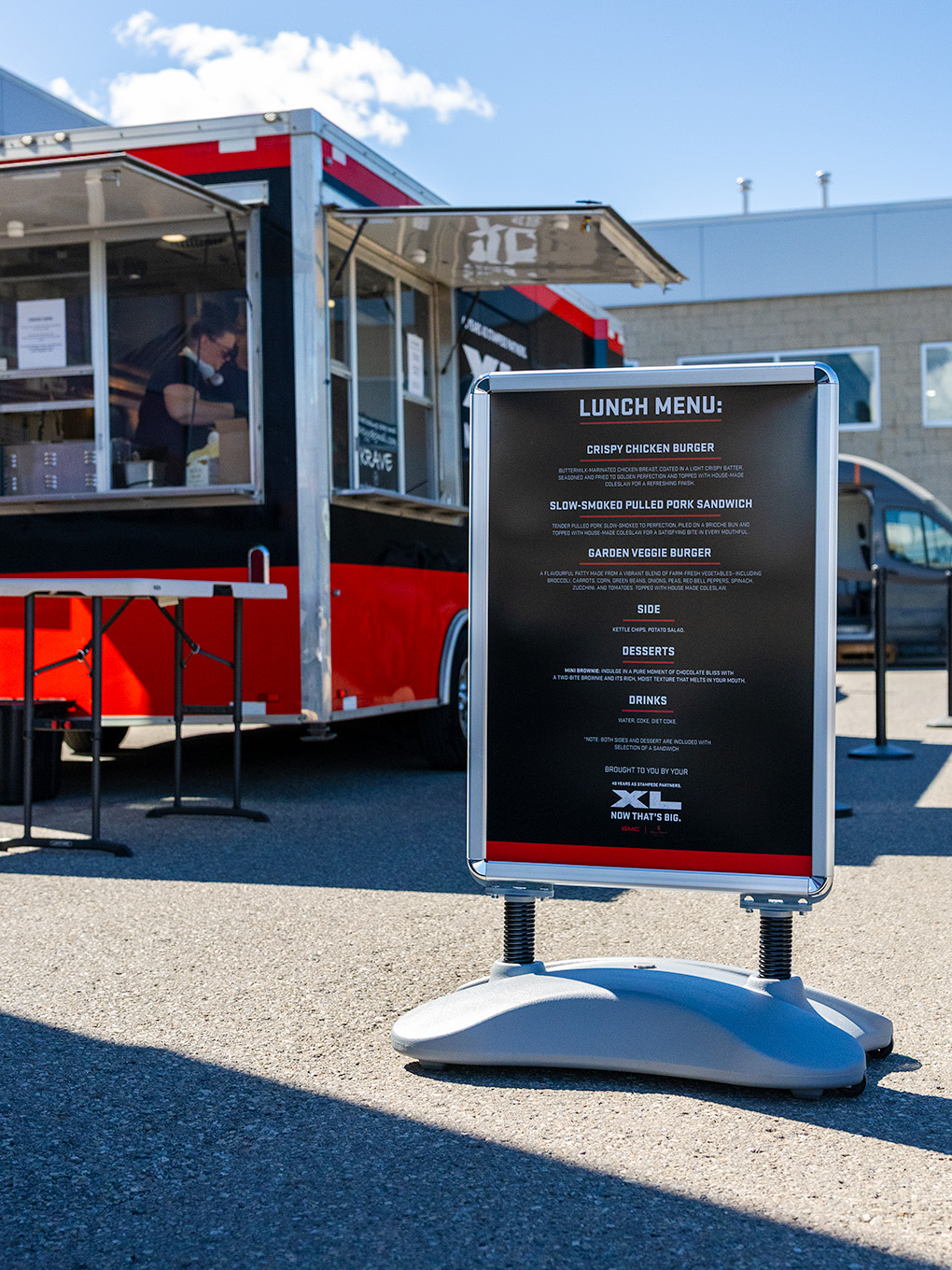 Lunch menu signage beside a custom-decaled GMC XL food trailer at a Stampede event.