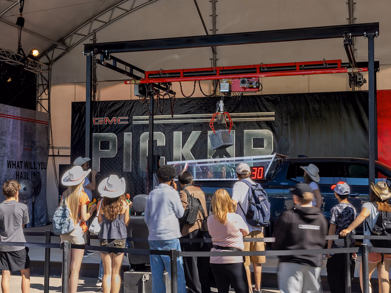 Crowd watches the claw crane lower toward a prize box in the GMC truck bed claw game.