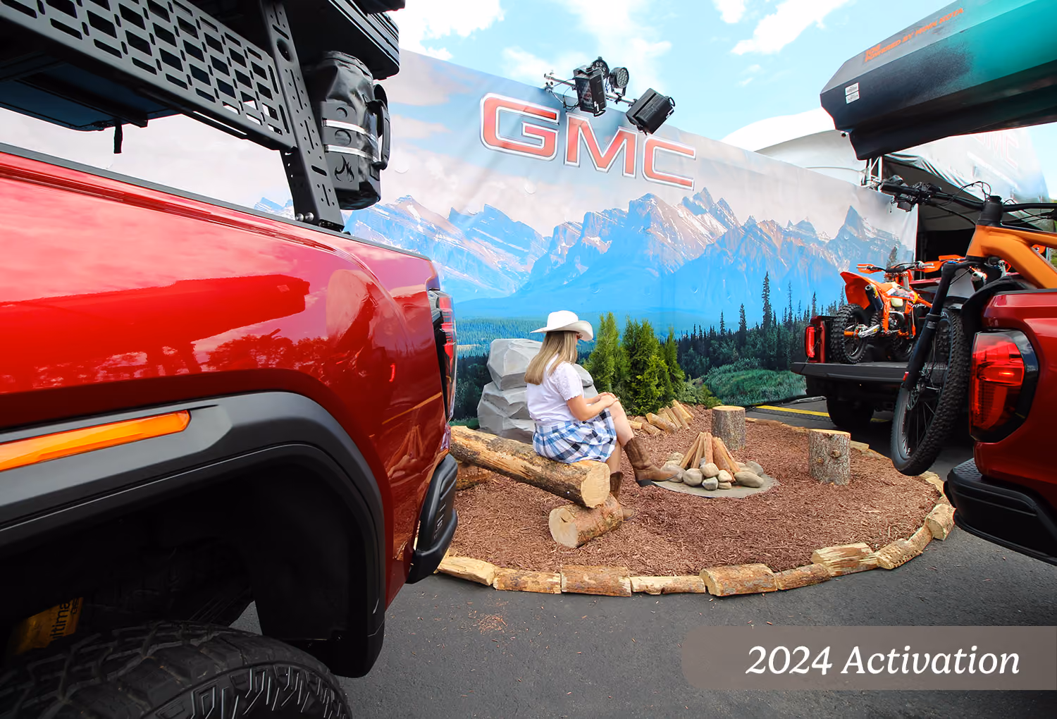 2024 custom campfire zone display with mountain backdrop graphic between two GMC trucks.