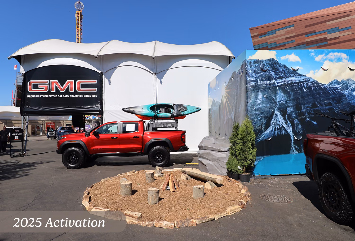 2025 campfire zone display with mountain backdrop, kayak-equipped GMC truck, and midway tent.