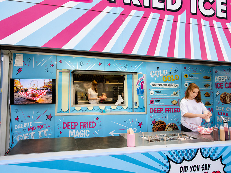Frio Frio's service window and topping counter, framed by playful blue menu graphics that read "Deep fried magic" and "One bite and you'll get it."