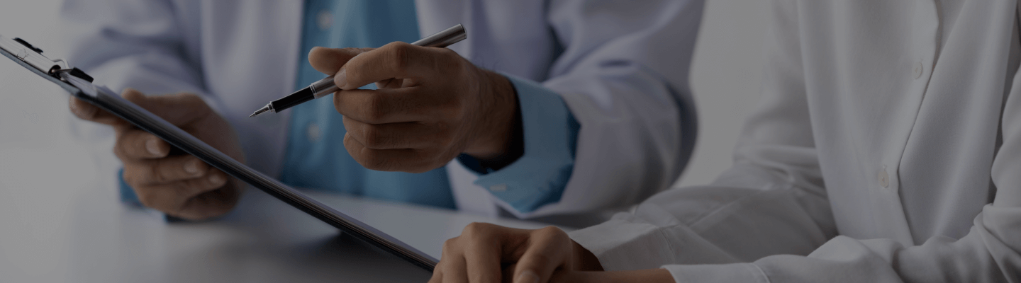 Medical professionals reviewing a clipboard with documents, one holding a pen pointing at the papers.