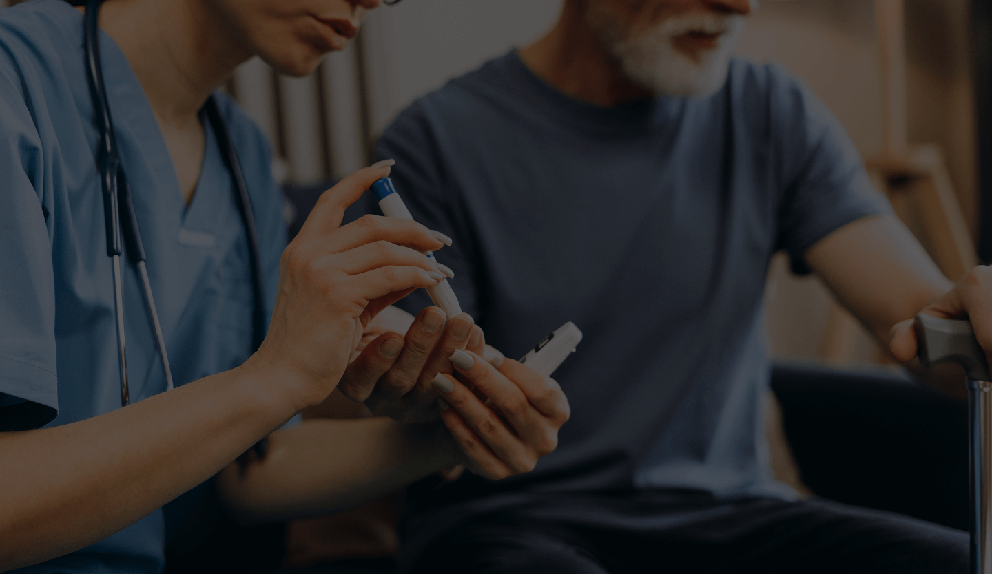 Healthcare professional demonstrating blood glucose monitoring to an elderly man holding a cane.