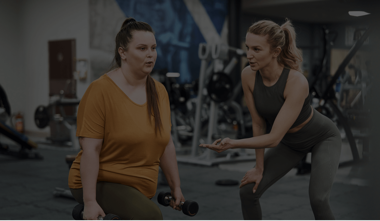 A fitness trainer coaching a woman holding dumbbells in a gym setting.