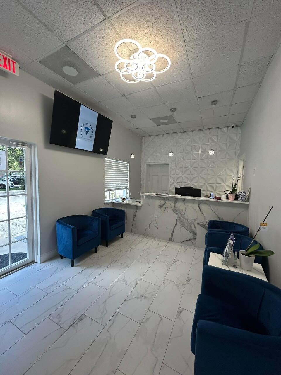 Modern waiting room with blue velvet chairs, a marble reception desk, textured white wall, and a ceiling light fixture of overlapping rings.