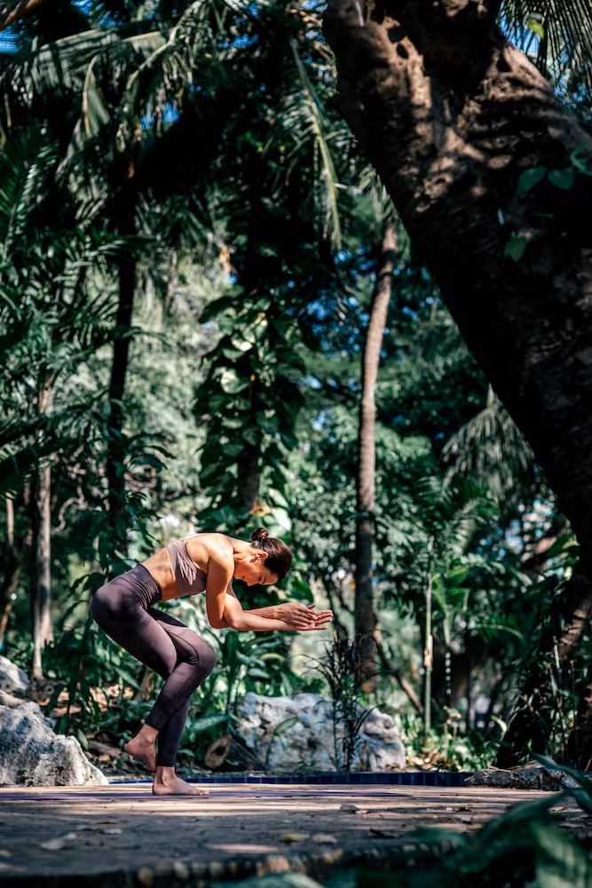A woman practices yoga in a lush tropical garden, bowing forward in balance and concentration—movement and stillness coexisting in natural harmony.
