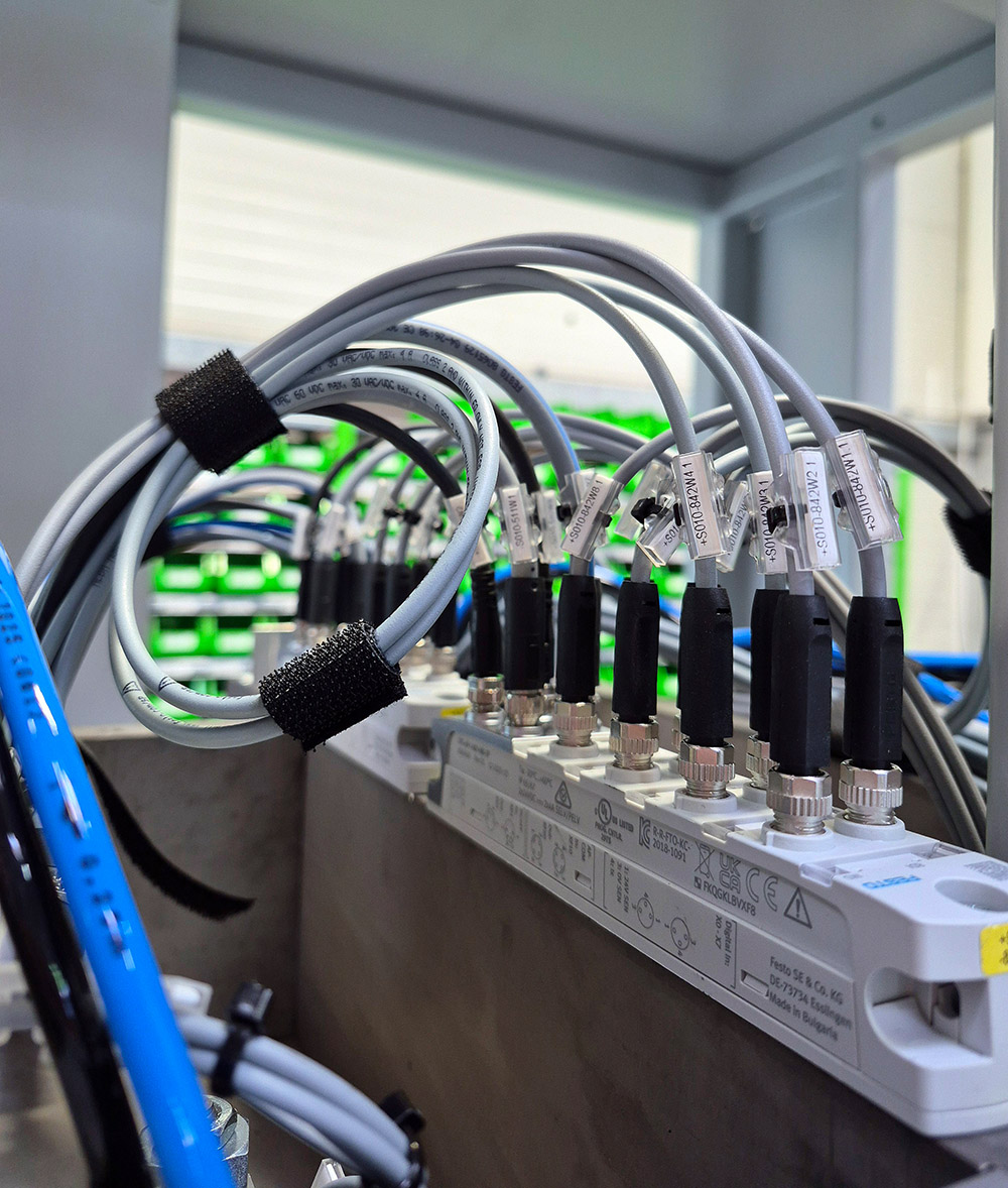Verschiedene graue Kabel sind mit schwarzen Steckverbindungen an einem weißen Gerät angeschlossen.