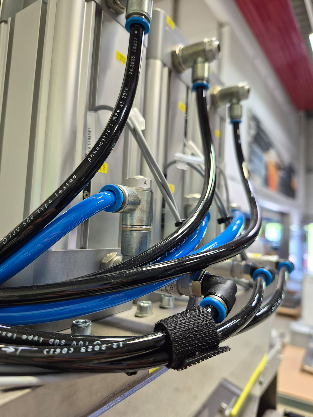 Schwarze und blaue Pneumatikschläuche, die an einer metallischen Maschine in einer Fabrik befestigt sind.