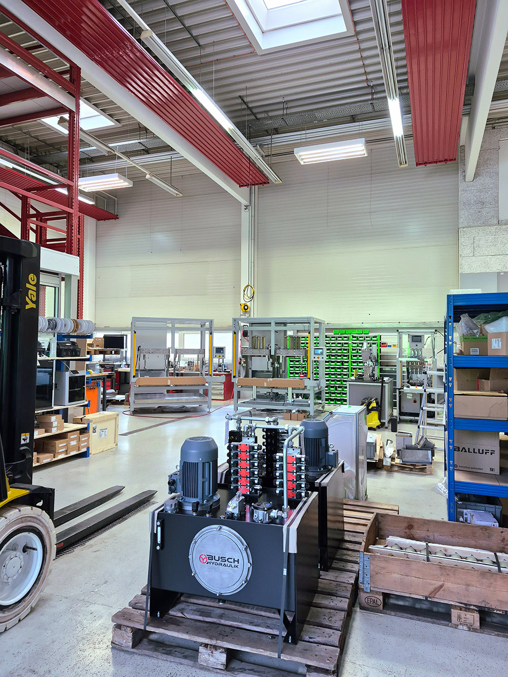 Industrielle Hydraulikanlagen auf Paletten in einer modernen Werkstatt mit Regalen und Maschinen.