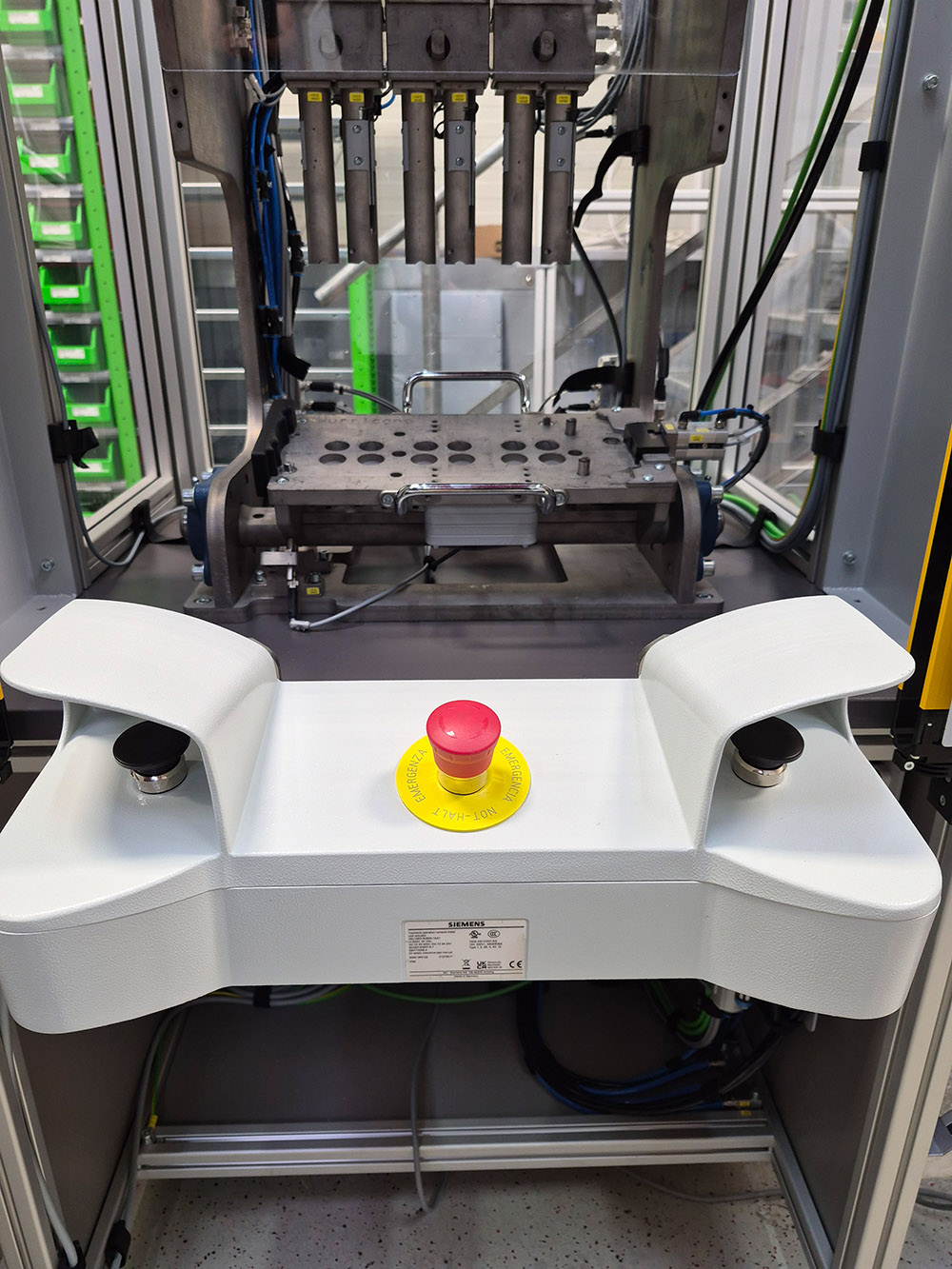 Industriemaschine mit rotem Not-Aus-Knopf in der Mitte und Metallsteuerung im Hintergrund.