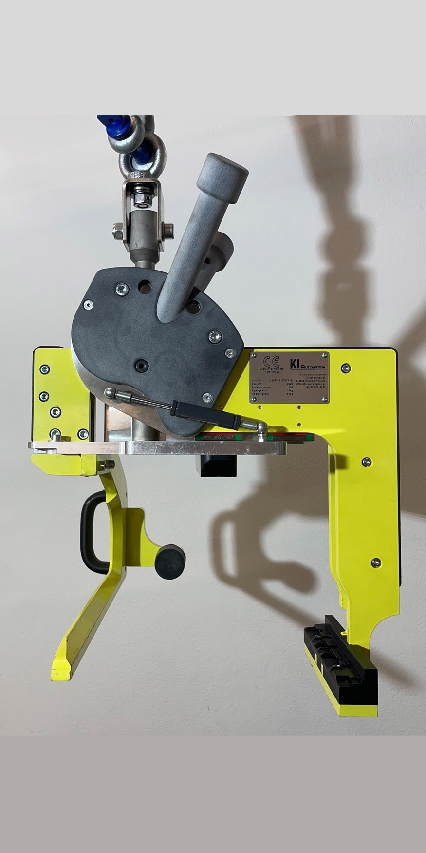 Gelbes mechanisches Gerät mit Hebel, Handgriff und Metallplakette an weißer Wand.