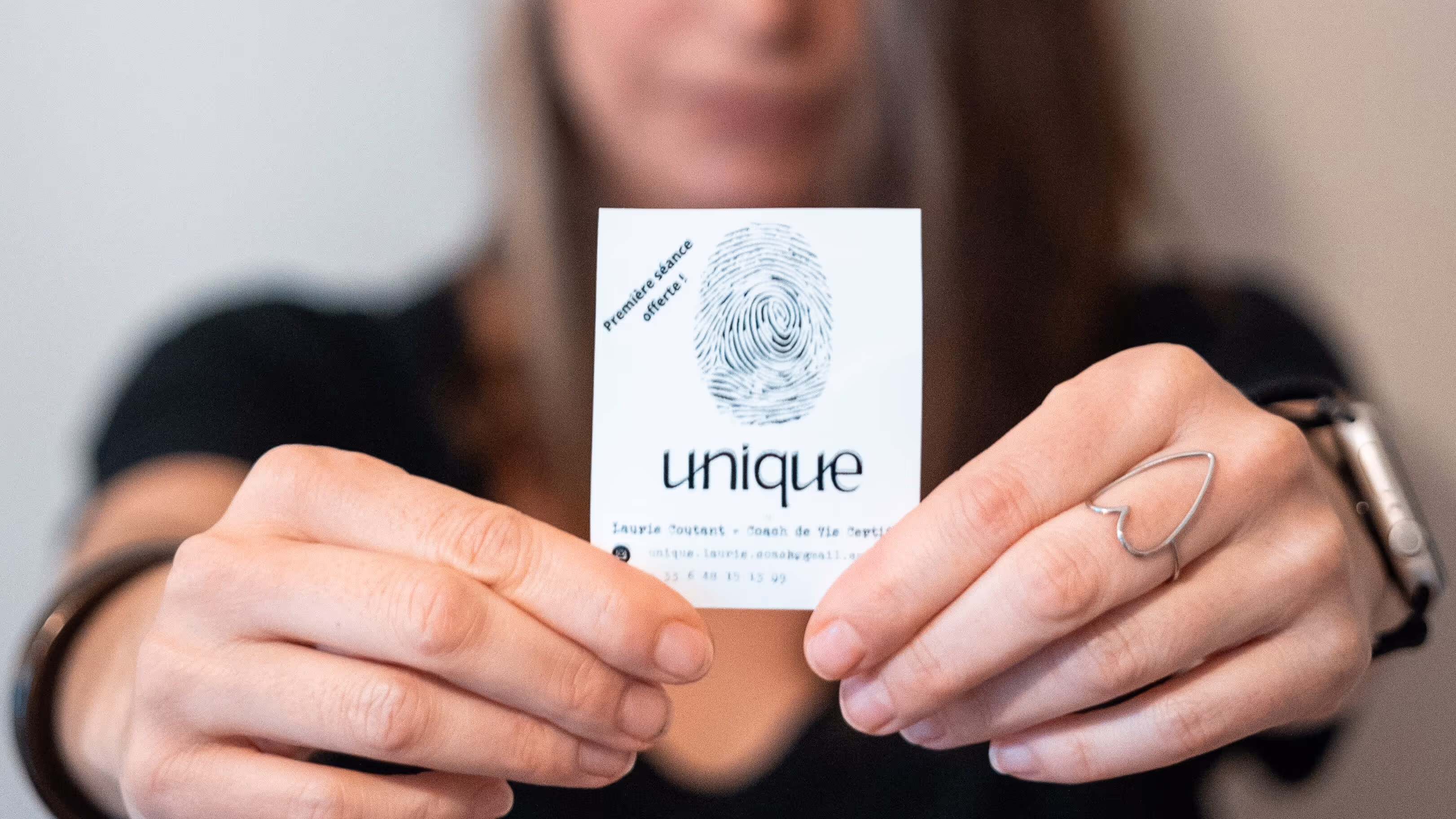 Mains tenant une carte de visite blanche avec une empreinte digitale et le texte « unique » et « Première séance offerte ! ».