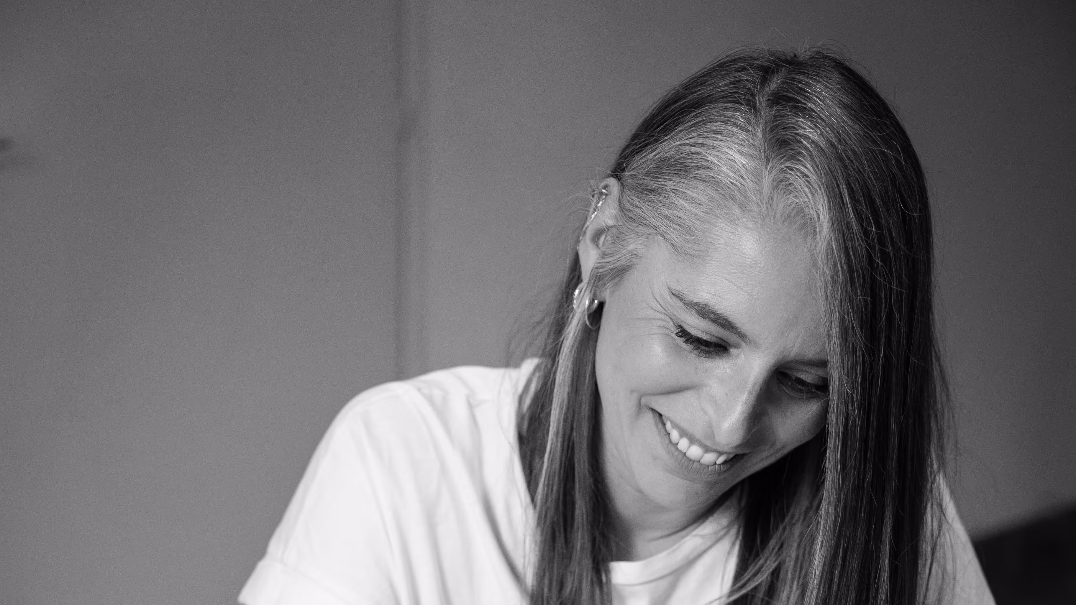 Portrait d'une femme brune souriante en noir et blanc regardant vers le bas sur une table de bureau.