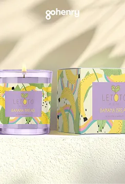 Lit purple candle and matching box with colorful banana bread-themed design and lemon illustrations.