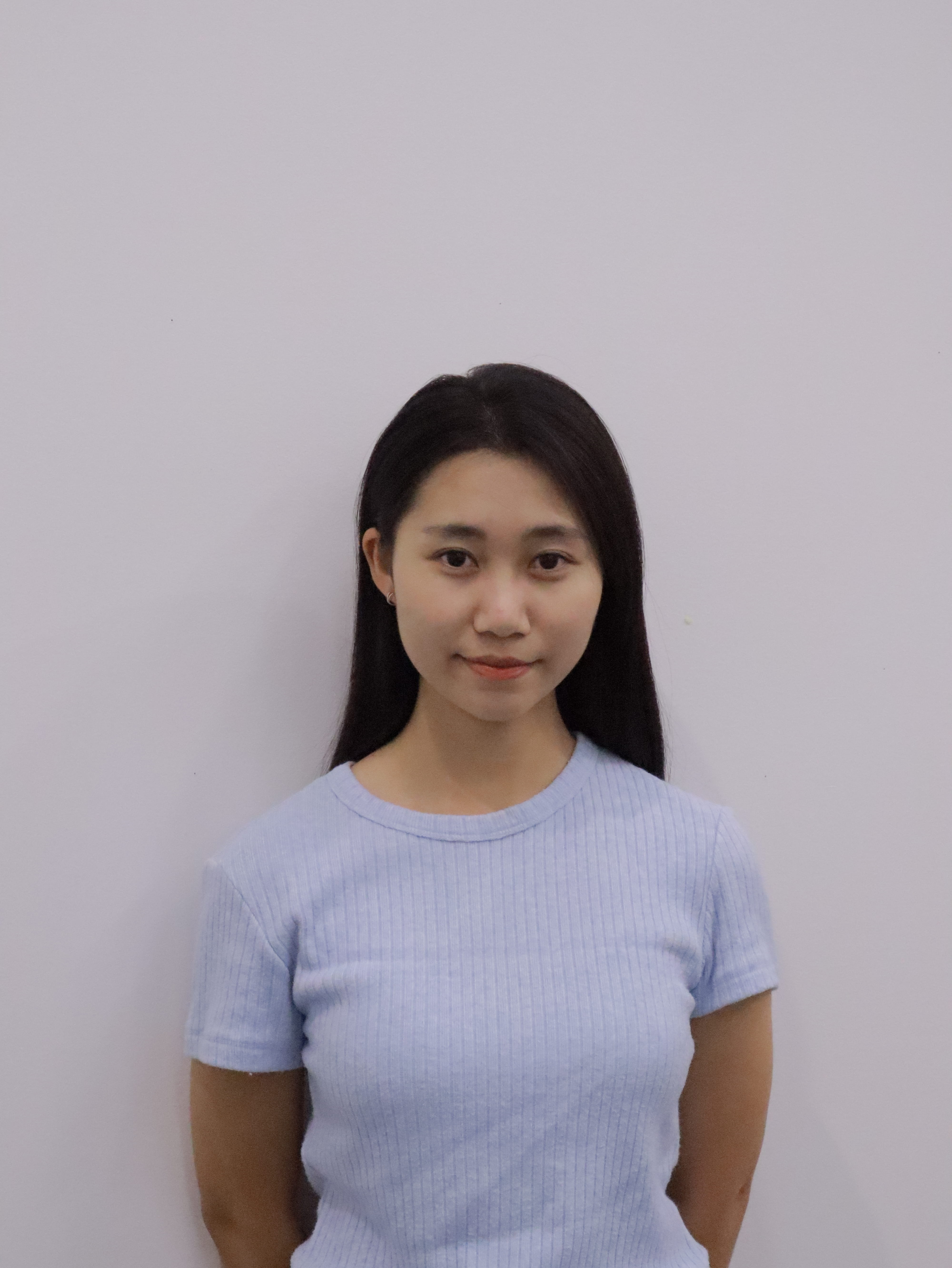 Smiling young woman with long dark hair wearing a denim jacket and light gray shirt against a plain beige background.