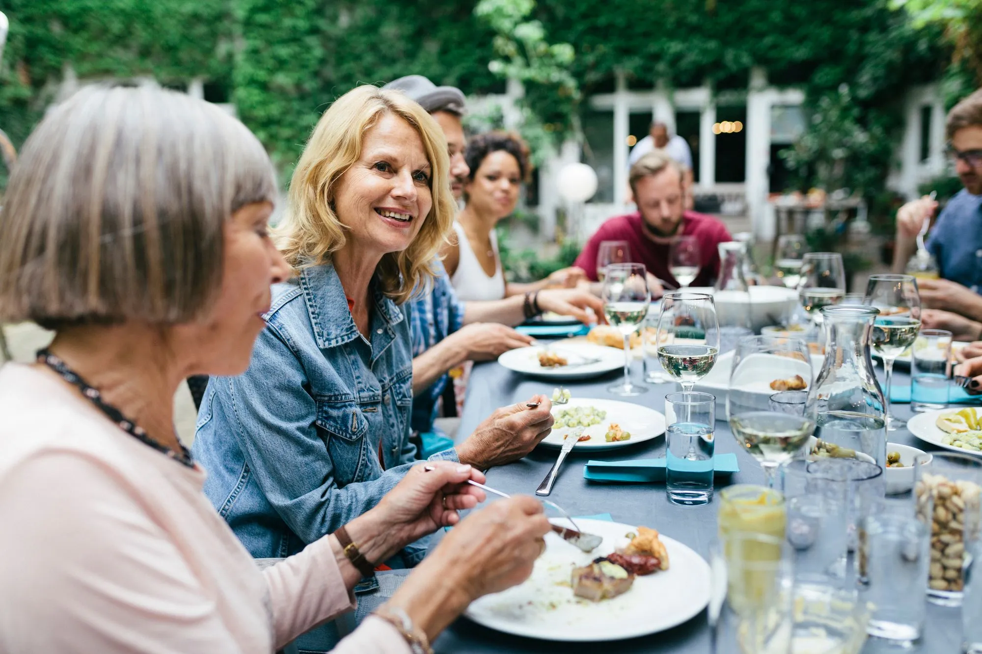 a large group of people sitting around an outdoors table eating food and enjoying themselves