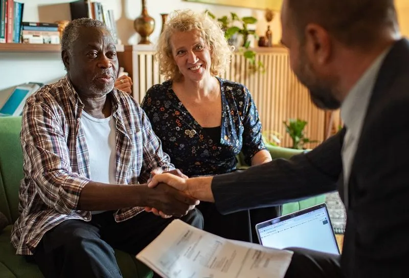 A lawyer leaning across and shaking the hand of a man who is sitting next to his wife.
