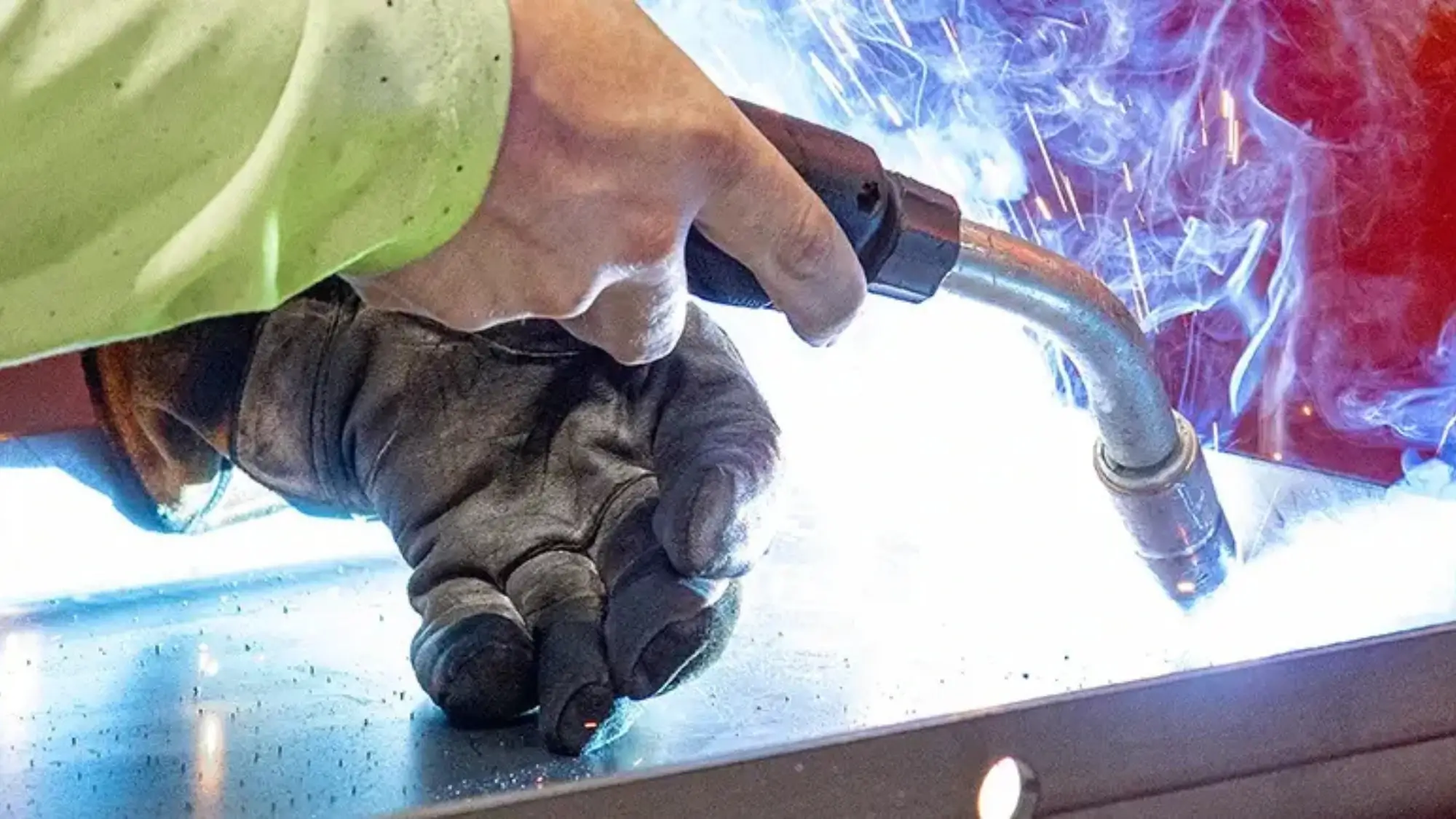 Metalworker welding a steel surface with bright sparks and protective gloves, showcasing precision fabrication and industrial craftsmanship.