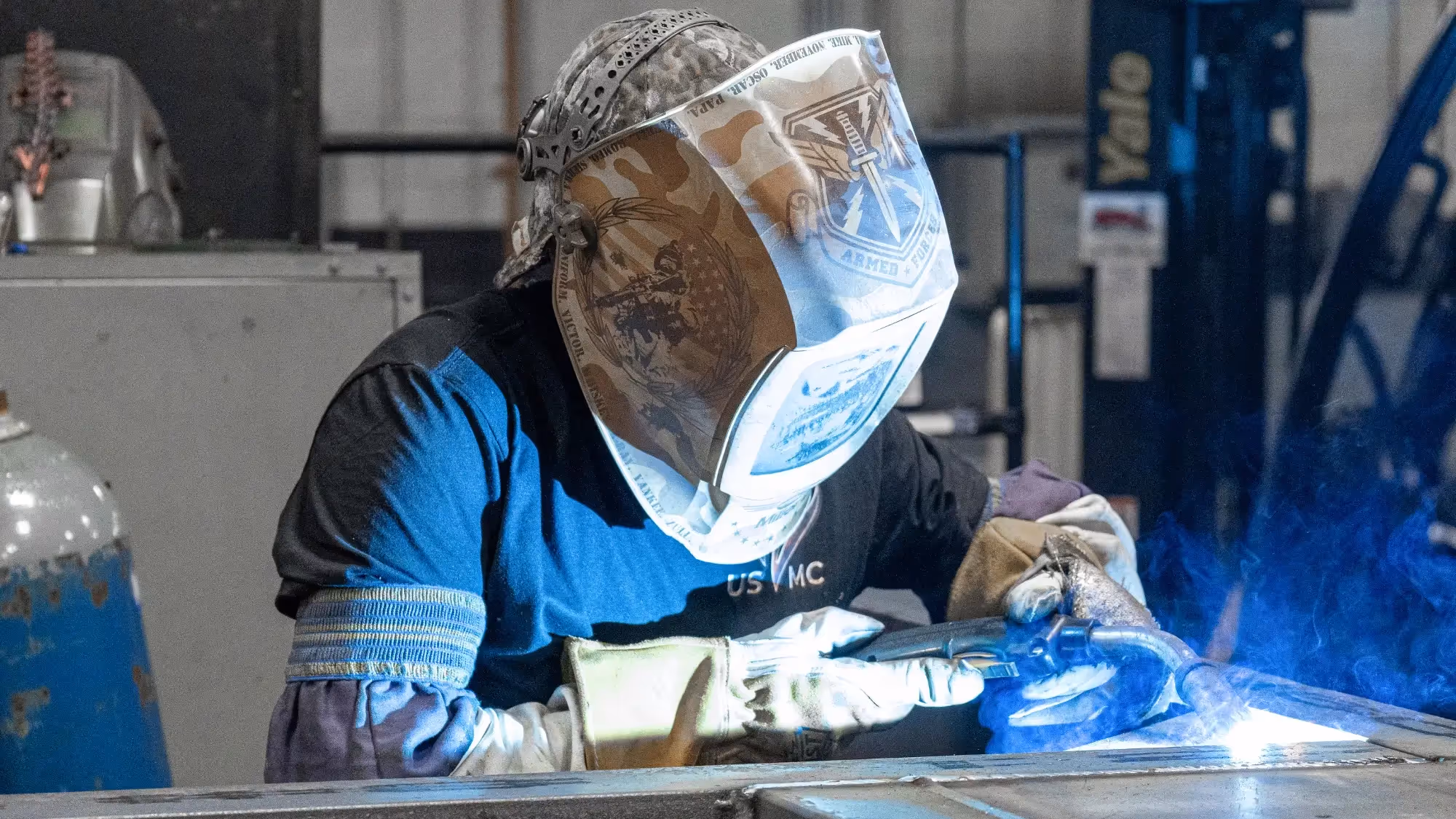 Welder in protective gear carefully fuses metal with bright blue sparks, highlighting skilled craftsmanship and industrial precision.